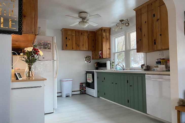 Cozy kitchen with wooden cabinets, green lower cabinets, white appliances, and a vase of flowers on the counter.