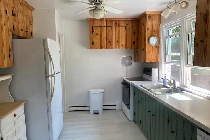 Bright kitchen featuring wooden cabinets, white appliances, green lower cabinets, and a window with natural light.