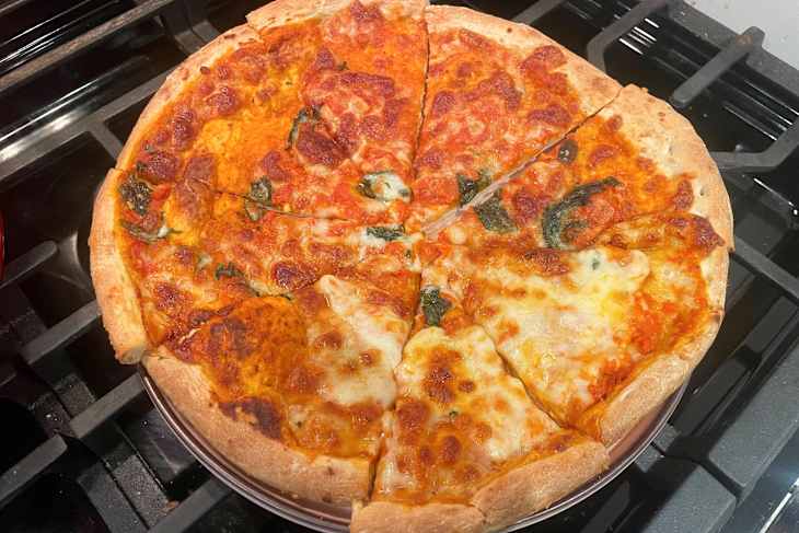 Cheese and tomato pizza with spinach, sliced into eight pieces, on a stovetop.