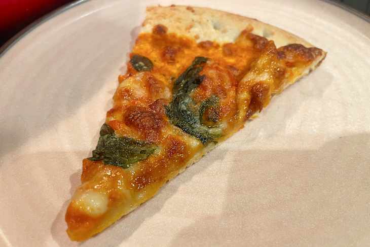 Slice of pizza topped with melted cheese and green spinach on a beige plate.