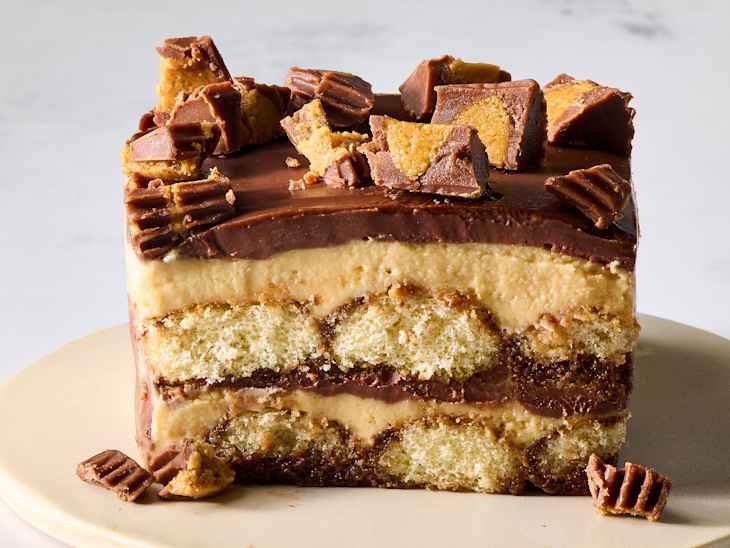chocolate peanut butter tiramisu with chocolate and peanut butter frosting, topped with chopped candy pieces, on a cream plate.