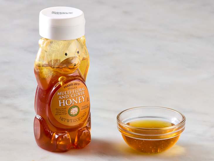 Honey bear bottle filled with multi-floral and clover honey next to a small glass bowl of honey.