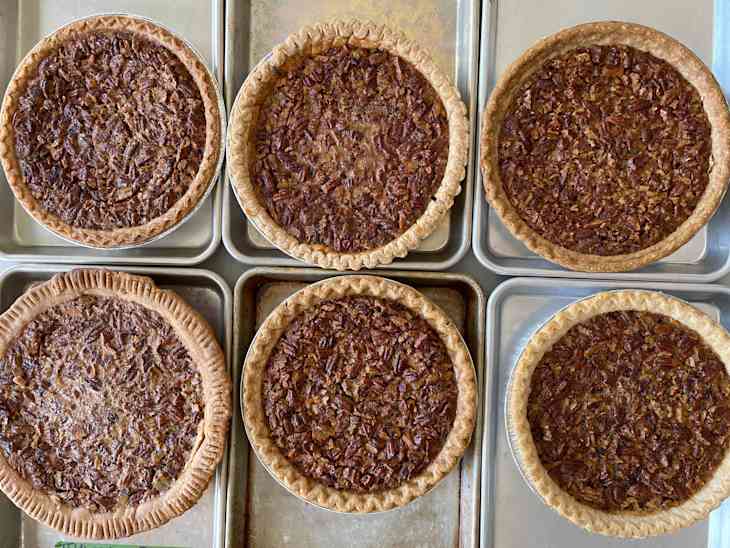 6 pecan pies on baking trays with parchment paper each with different thickness texture and color of crust