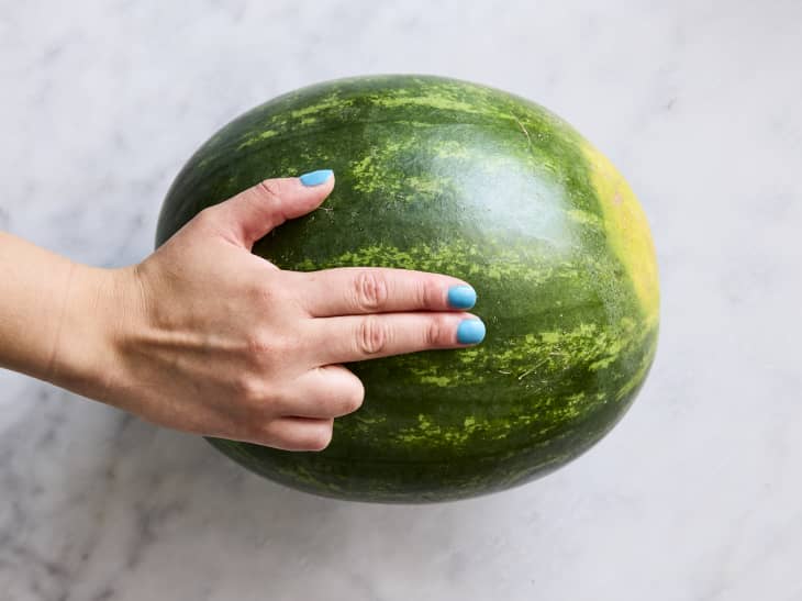 overhead shot of a hand on top of a watermelon, using the two finger trick.