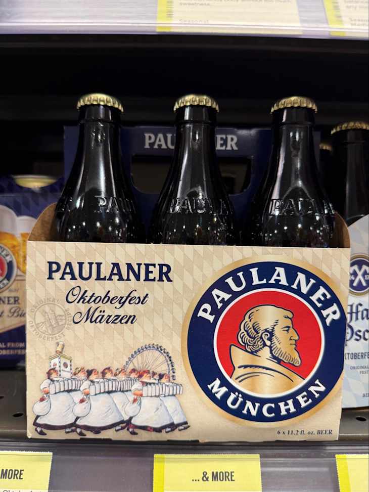 Six-pack of Paulaner Oktoberfest Märzen beer with a colorful label featuring traditional dancers and a ferris wheel.