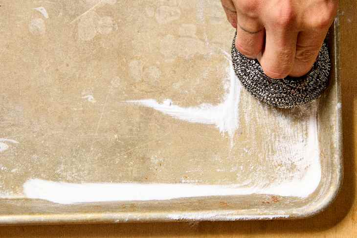 overhead shot of someone removing the rust from a sheet pan using a steel wool pad