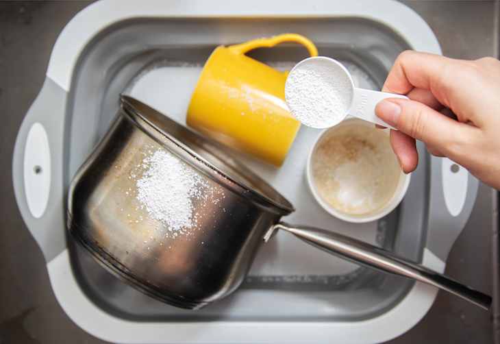 a measuring spoon with granules of environmentally friendly oxygen bleach is in the girl s hand. A modern means for cleaning and washing dirty dishes.
