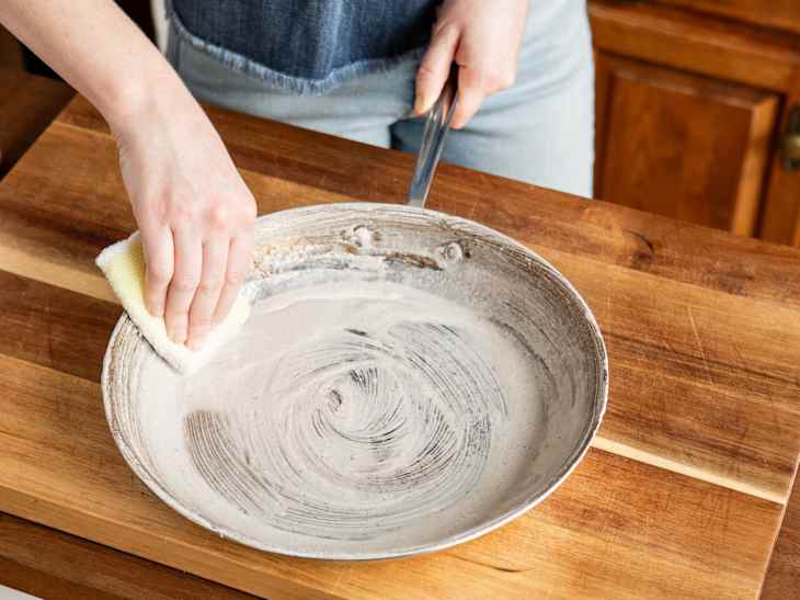 Someone scrubbing inside of All-Clad skillet with Bar Keepers Friend.