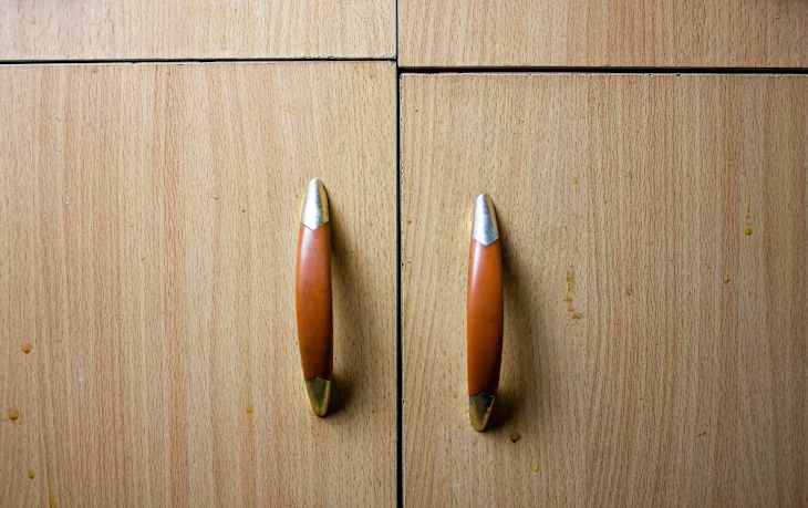 The Old uneven cabinet doors with handles. Broken, dilapidated crooked furniture cabinet with handles close-up background.