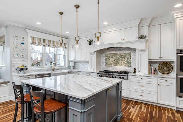 ELMHURST, IL, USA - JANUARY 30, 2020: A luxurious, white kitchen with a granite counter top and a tiled backsplash behind the stainless steel KitchenAid stovetop.