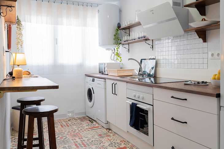 Modern kitchen with white cabinets, wooden countertop, washing machine, and decorative tiles on the floor.