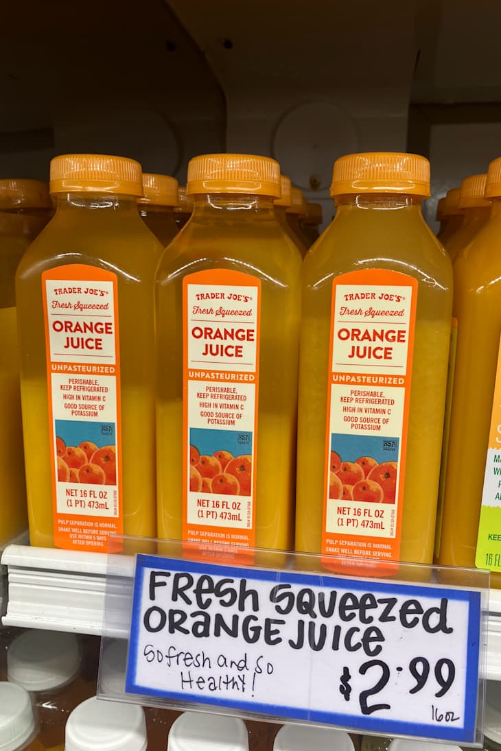 Bottles of Trader Joe's fresh squeezed orange juice on a shelf.