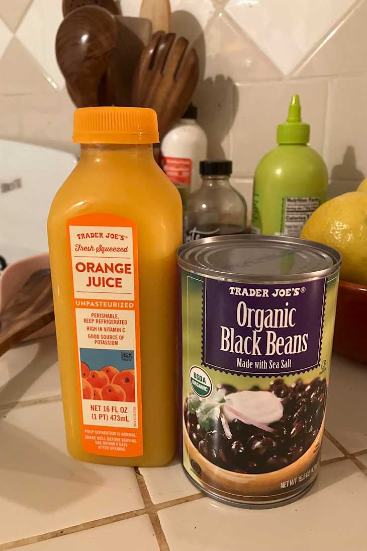 A bottle of orange juice and a can of organic black beans on a kitchen counter.