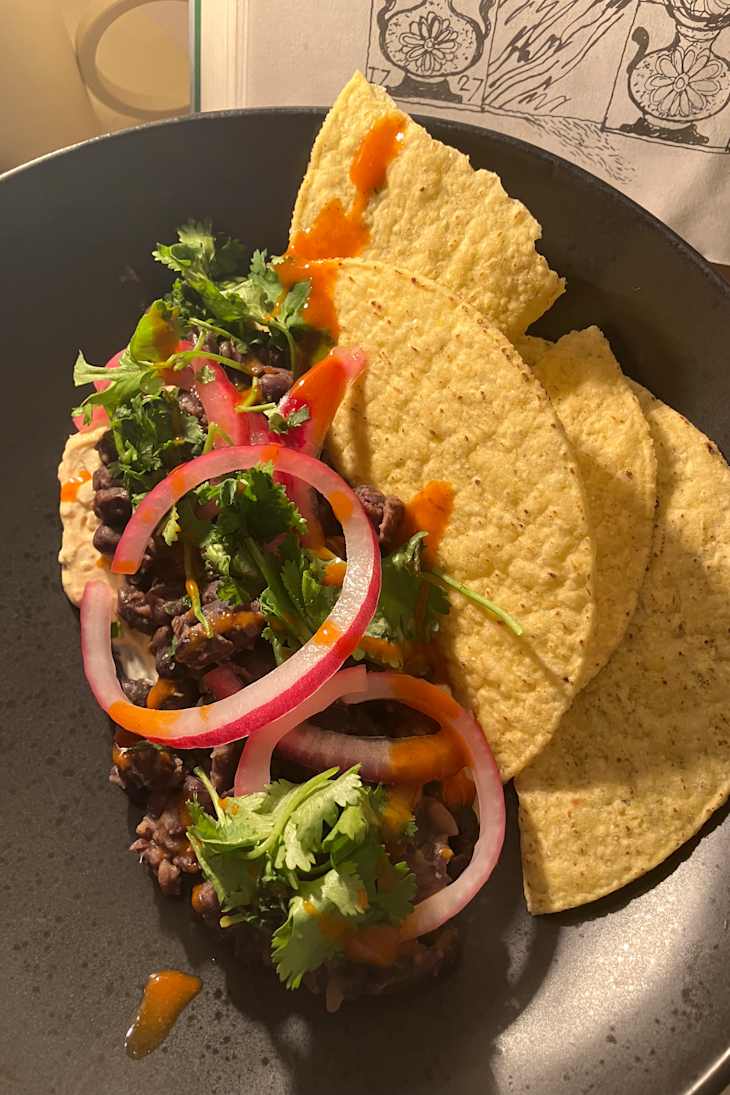 Black beans topped with cilantro, pickled onions, and sauce, served with tortilla chips.