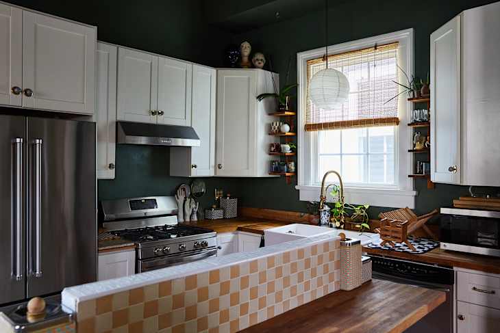 Modern kitchen with dark green walls, white cabinets, stainless steel appliances, wooden countertops, and decorative plants.