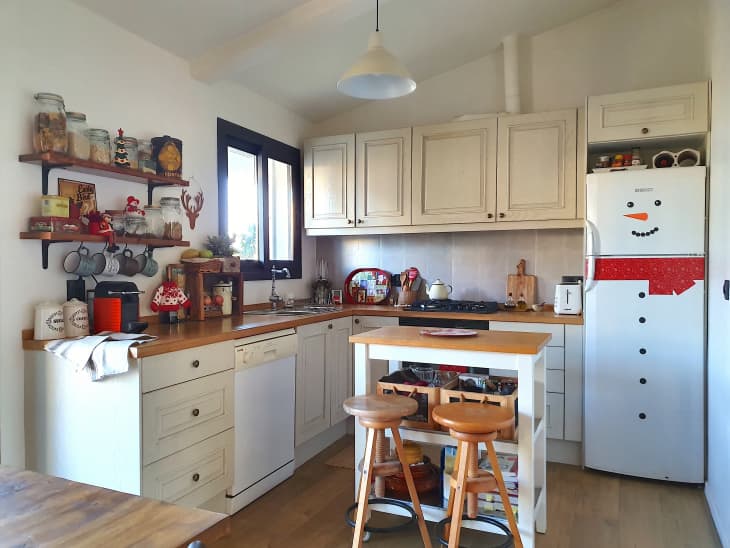 Cozy kitchen with wooden countertops, shelves with jars, a snowman-themed fridge, and a small island with stools.