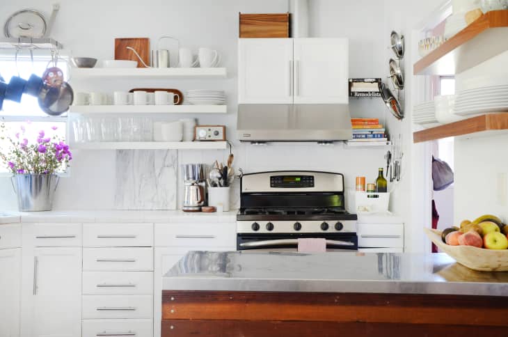 A mostly white kitchen with medium wood accents throughout and a black and stainless steel stove