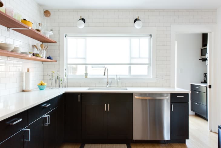 Modern kitchen with black cabinets, white countertops, open wooden shelves, and stainless steel dishwasher.