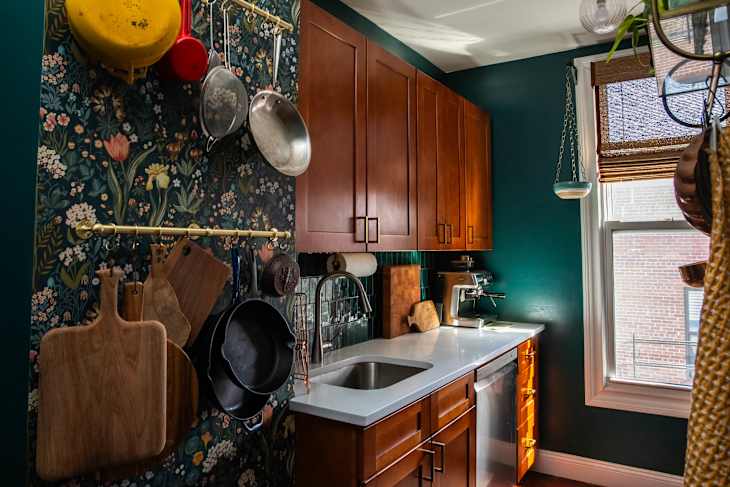 Cozy kitchen with dark green walls, wooden cabinets, hanging cookware, and a white countertop with a sink.