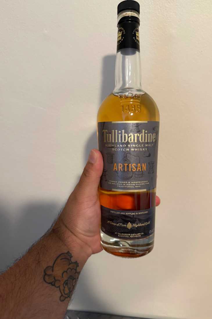 A person holding a bottle of Tullibardine Artisan Highland Single Malt Scotch Whisky.