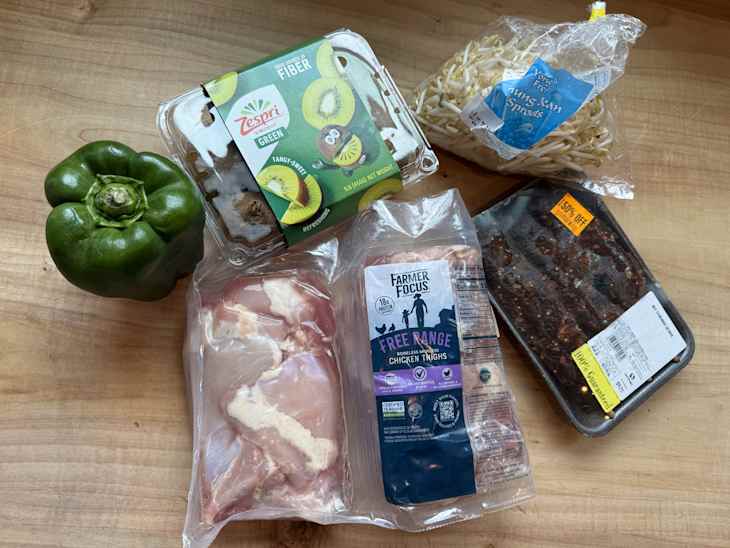 Green bell pepper, kiwi container, bean sprouts, chicken thighs, and marinated chicken on a wooden surface.