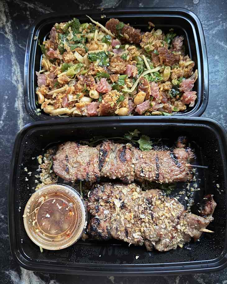 Grilled meat skewers with herbs and a dipping sauce, served alongside a salad with peanuts and greens.