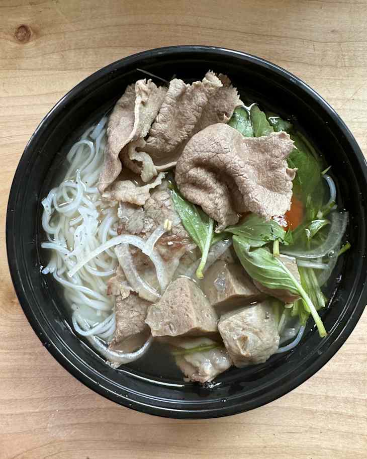 Bowl of pho with rice noodles, slices of beef, fresh herbs, and onions in clear broth.