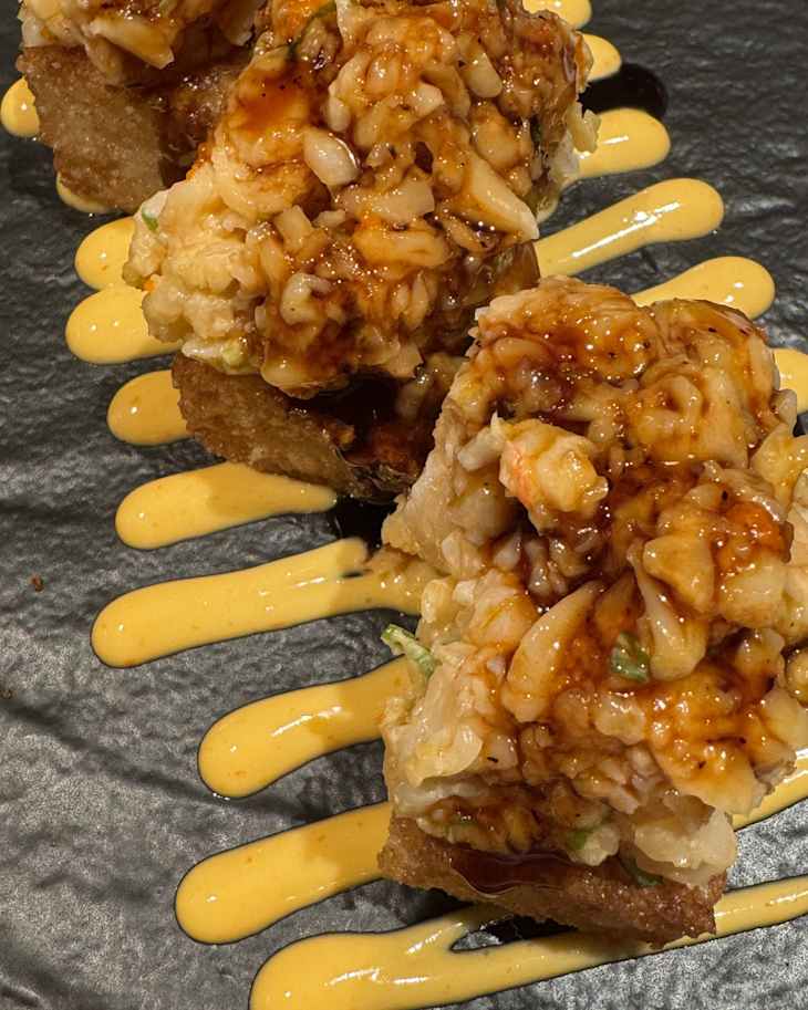 Crispy rice topped with a savory seafood mixture and drizzled with a creamy sauce on a dark plate.