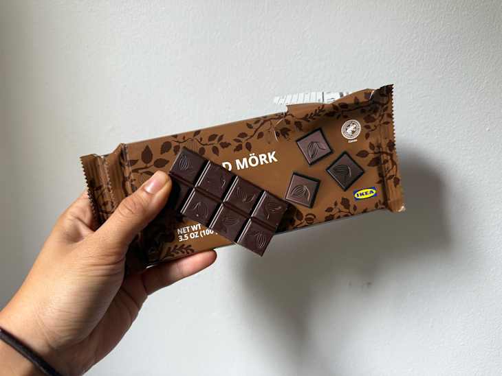 Someone holding up a piece of chocolate bar with wrapper behind.