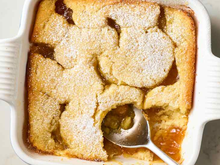 lemon cobbler with a golden crust, powdered sugar topping, and a spoon revealing fruit filling underneath.