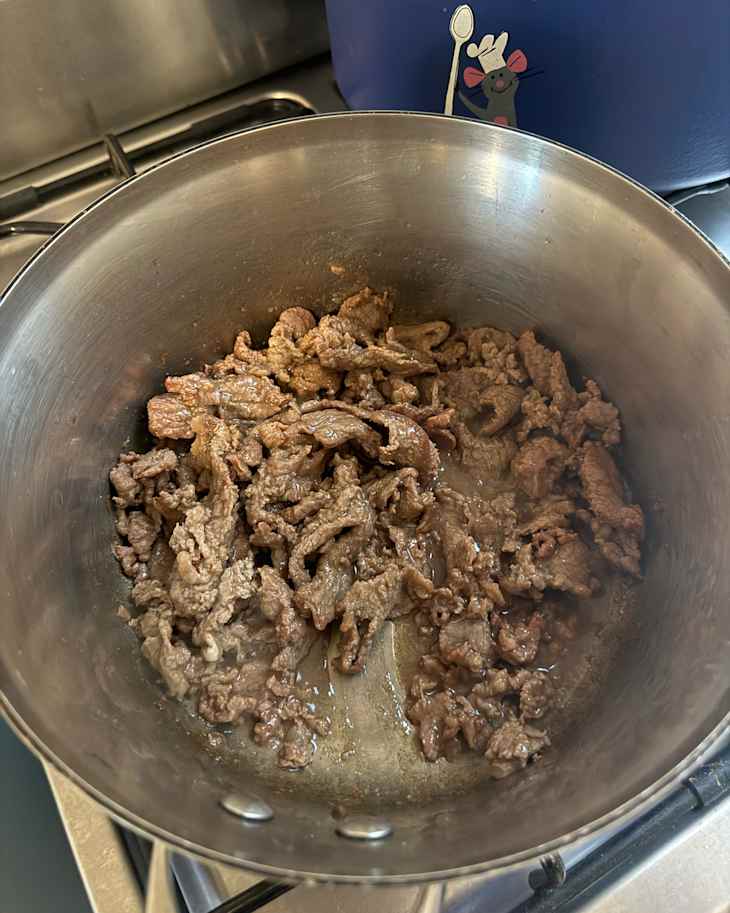 Beef strips cooking in pot.