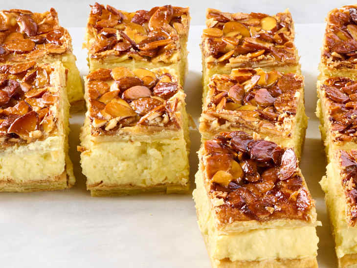 Angled photo of bee sting dessert bars showing the caramelized sliced almond topping, the pudding center, and the flaky puff pastry bottom and top layers.