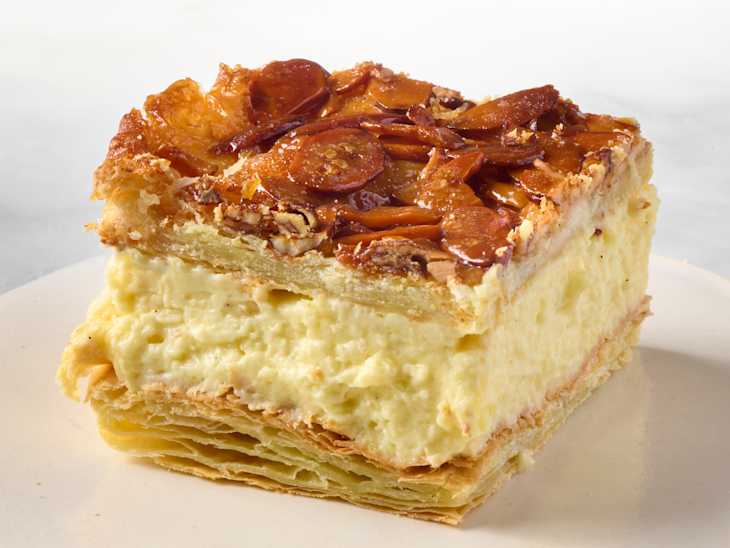 Angled photo of one bee sting dessert bar showing the caramelized sliced almond topping, the pudding center, and the flaky puff pastry bottom and top layers.