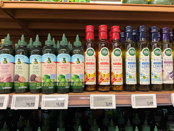 Bottles of flavored olive oils on a shelf, including roasted garlic, black truffle, jalapeño herb, and various infused oils.