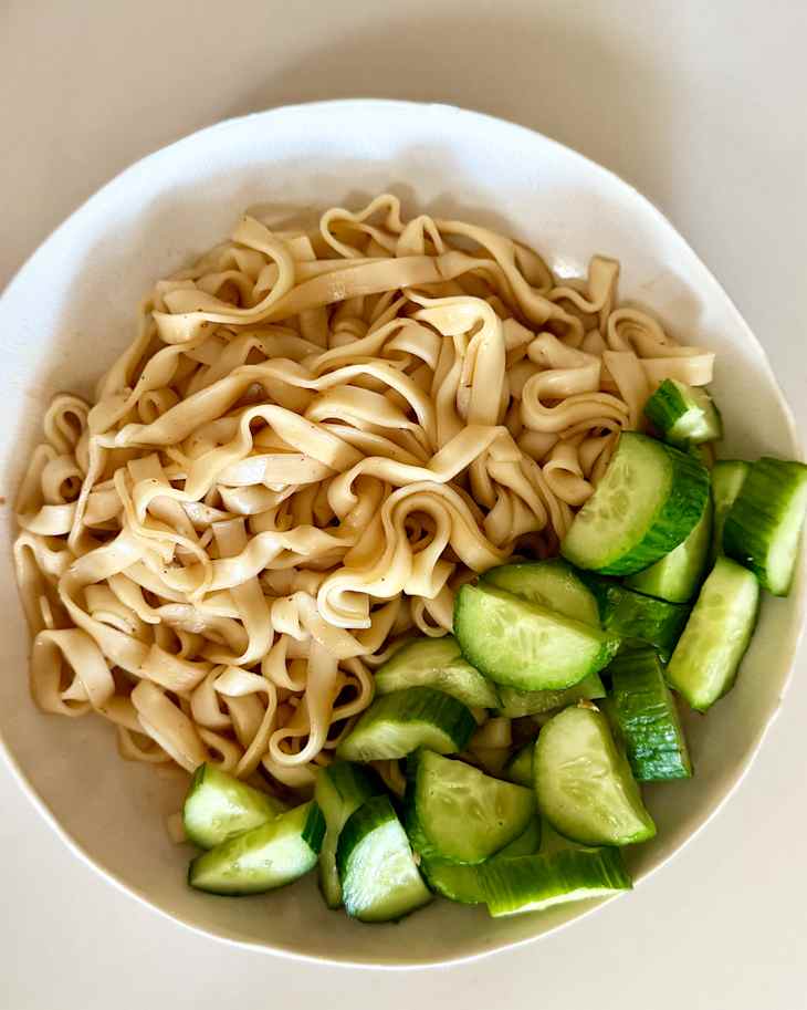 Noodles in bowl with side of cucumbers.
