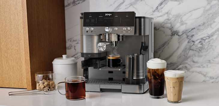 Coffee machine on a marble countertop with two drinks: iced coffee and iced latte, alongside a glass jar of cookies.