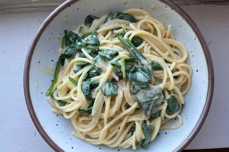 Pasta with spinach in a creamy sauce served in a speckled bowl.