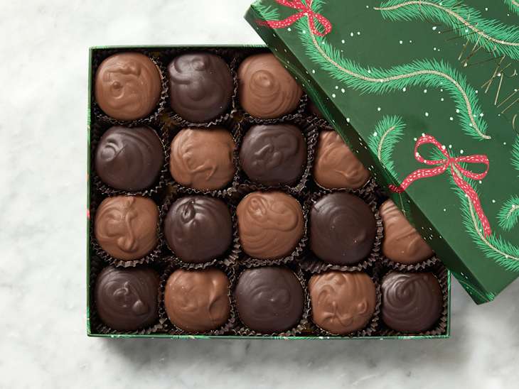 Box of assorted chocolates with dark and milk chocolate pieces, decorated with a festive green lid featuring red ribbons and pine branches.