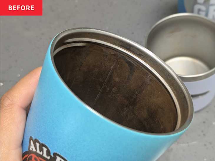 A hand holding a blue cup with a dirty interior, showing a silver rim, against a gray surface with another cup in the background.