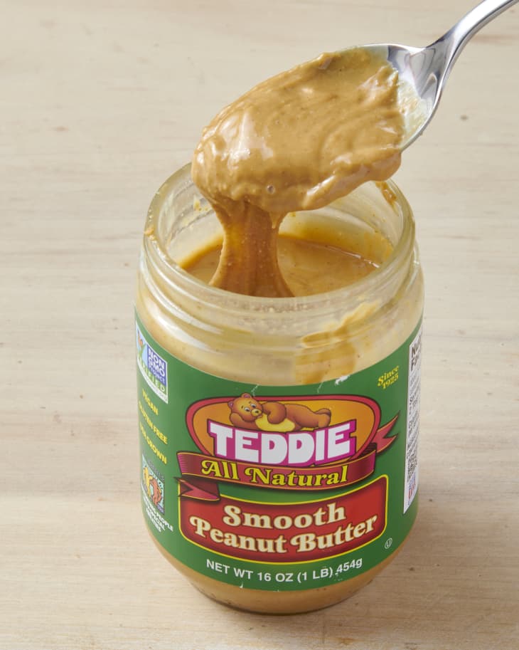 shot of a silver spoon with peanut butter from a peanut butter jar on a wooden surface