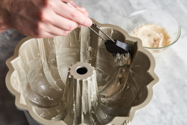 someone rubbing cake goop onto a bundt cake pan