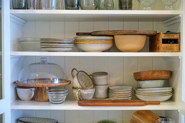 Filling the kitchen cabinet with clean dishes, plates and cups