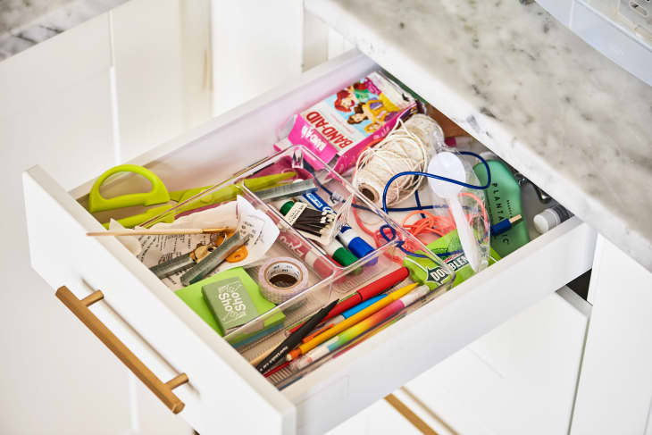 Open kitchen drawer with assorted items: scissors, pens, string, tape, markers, and a pack of gum.