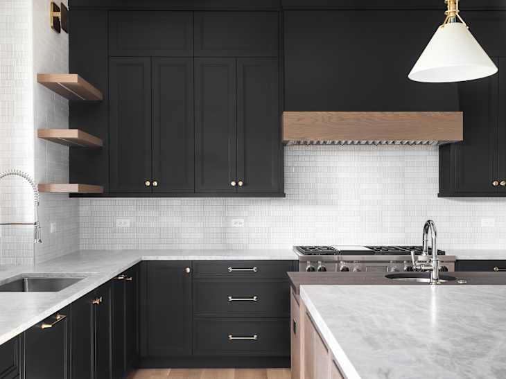 ELMHURST, IL, USA - OCTOBER 2, 2020: A luxury kitchen with black cabinets, granite counter top, tiled backsplash, stainless steel appliances, and chrome faucets.