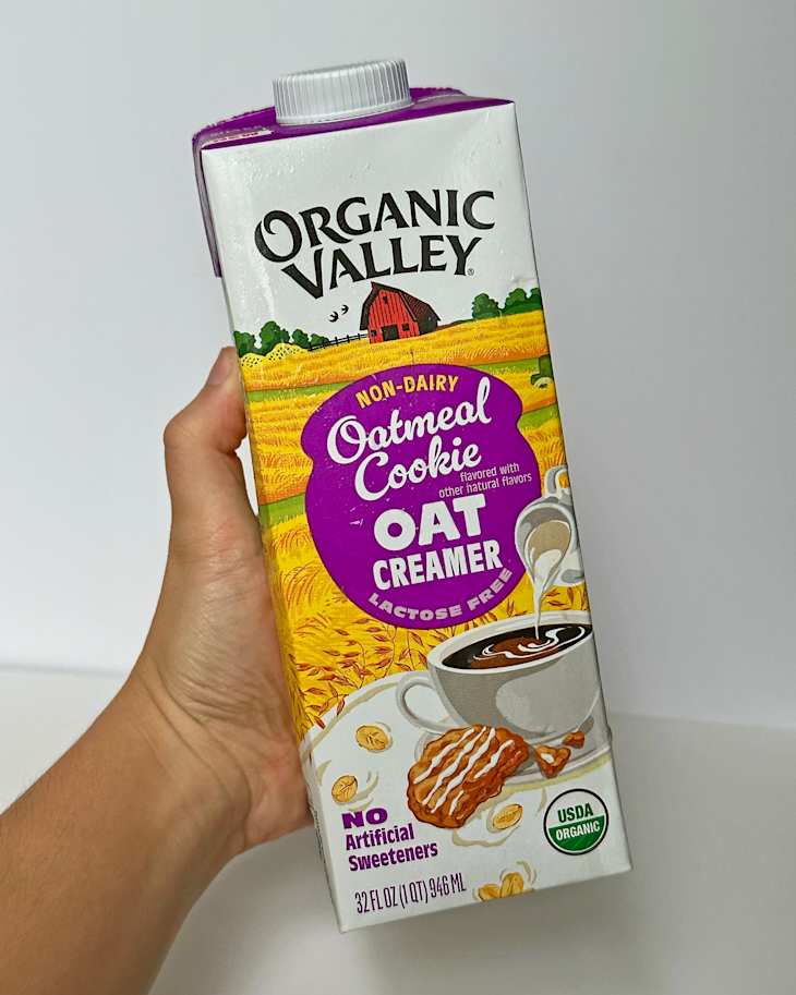 Non-dairy oatmeal cookie oat creamer carton held in hand, featuring a coffee cup and cookie illustration.