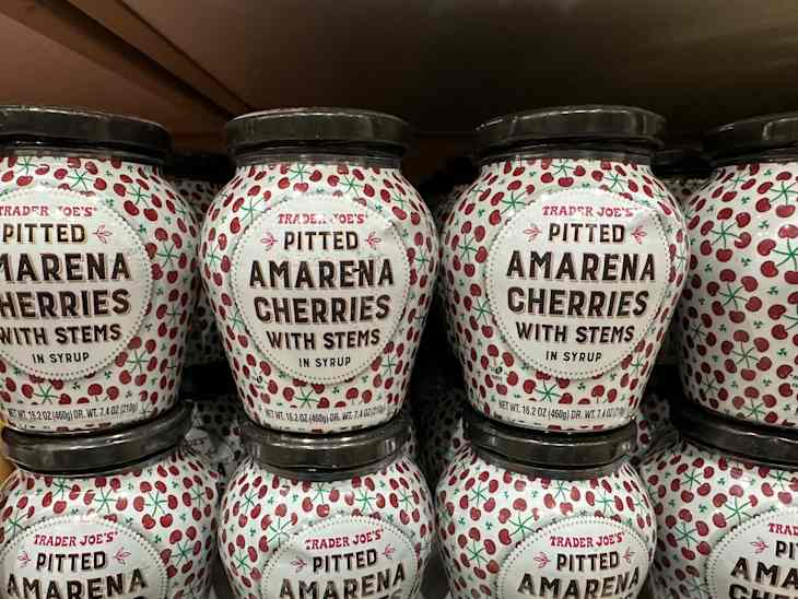 Jars of Trader Joe's Pitted Amarena Cherries with stems in syrup, decorated with a cherry pattern.