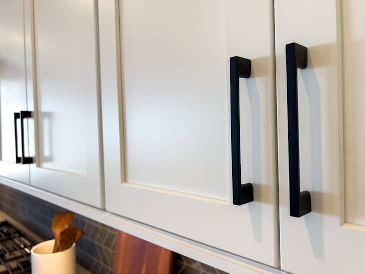 View of black vertical pulls on white kitchen cabinets. Neutral kitchen design with modern accents.