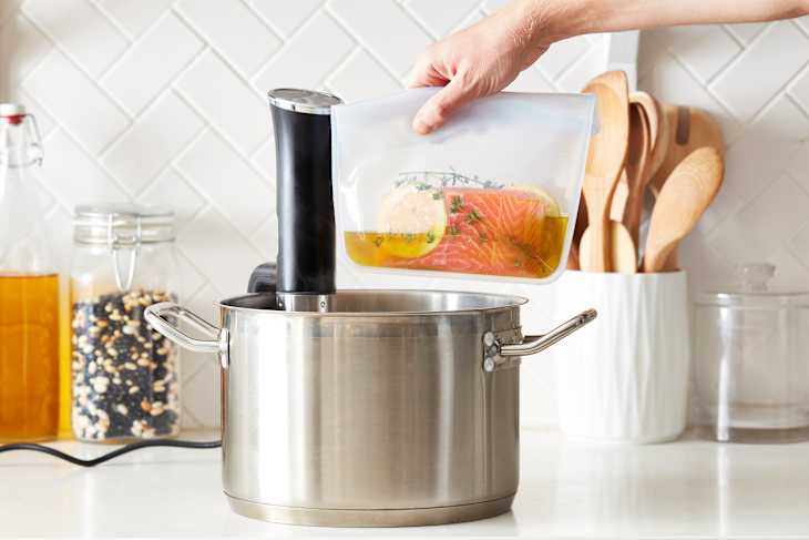 Sous vide salmon with lemon and herbs in a sealed bag being placed in a pot of water.