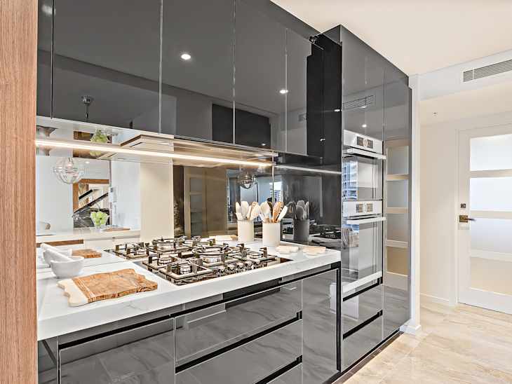 Black color pantry cupboards giving a shiny look beside the closed door. there are a stove and a kitchen utensils can be seen on the counter