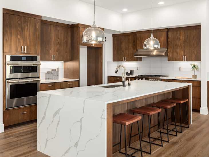 Kitchen in new luxury home with quartz waterfall island, hardwood floors, dark wood cabinets, and stainless steel appliances.